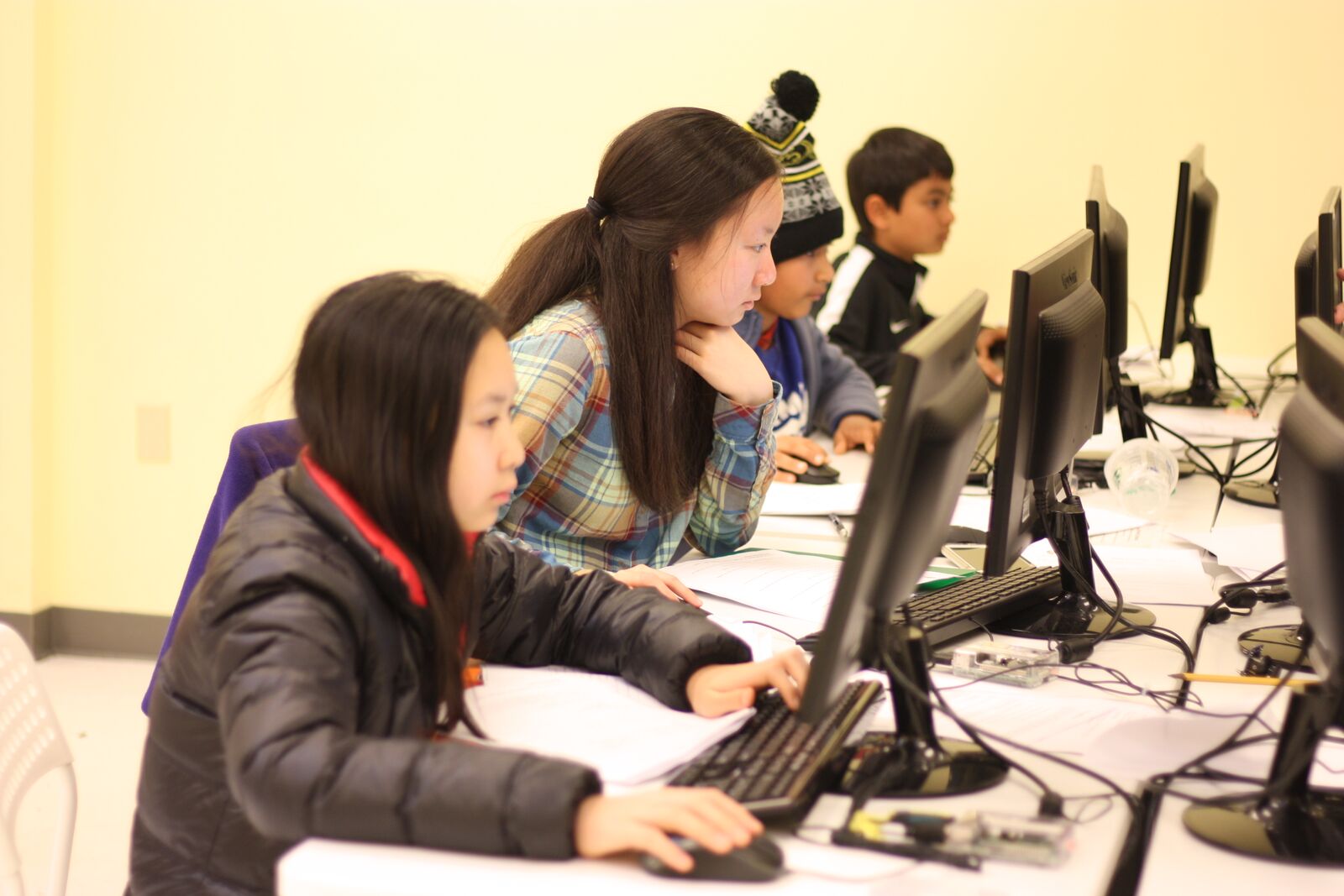 Kids and teens writing code on their computer and assisted by an experienced instructor.