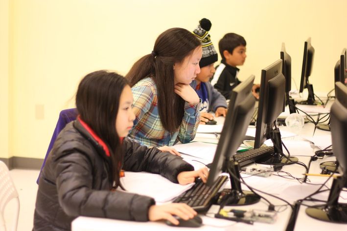 Kids and teens writing code on their computer and assisted by an experienced instructor.